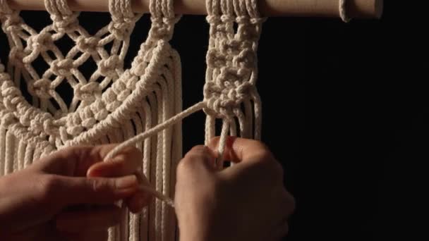 Donna tesse modello di fili di macrame con le proprie mani per la decorazione o l'arredamento domestico. Le mani delle donne legano nodi sulle corde in un laboratorio creativo su sfondo nero. Fatto a mano. Chiudete. Rallentatore. — Video Stock