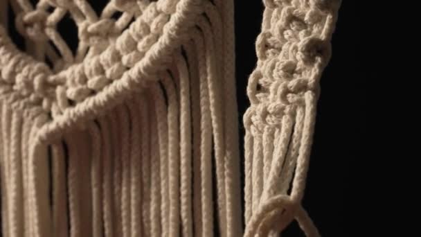 Woman weaves pattern of macrame threads with her own hands for decoration or home decor. Womans hands tying knots on ropes in a creative workshop on black background. Handmade. Close up. Slow motion. — Stock Video