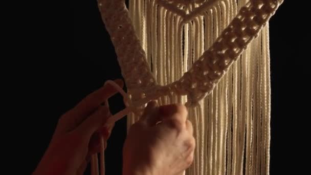 Womens hands weave a macrame pattern in creative workshop on black background. Woman ties knots on cotton threads to create lace. The base knots of macrame. Craft of rope. Close up. Slow motion. — Stock Video