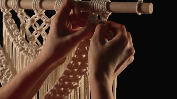 天然の白い綿の糸からマクラメのパターンを織ります。女性の手のニットは黒の背景にレースの装飾を作成します。ワークショップ、繊維工芸品の創造的なプロセス。閉めろ。スローモーション. — ストック動画