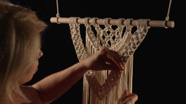 Tejer patrón de macramé a partir de hilos de algodón blanco natural. Las manos de las mujeres tejen nudos creando adornos de encaje sobre fondo negro. Proceso creativo en taller, artesanía textil. De cerca. Movimiento lento. — Vídeos de Stock