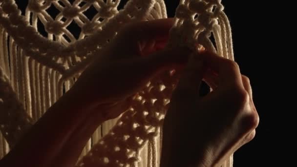 Țesut model macrame din fire de bumbac alb natural. Mâinile femeilor tricotează noduri creând ornament din dantelă pe fundal negru. Procesul creativ în atelier, meșteșuguri textile. De aproape. Slow motion. — Videoclip de stoc