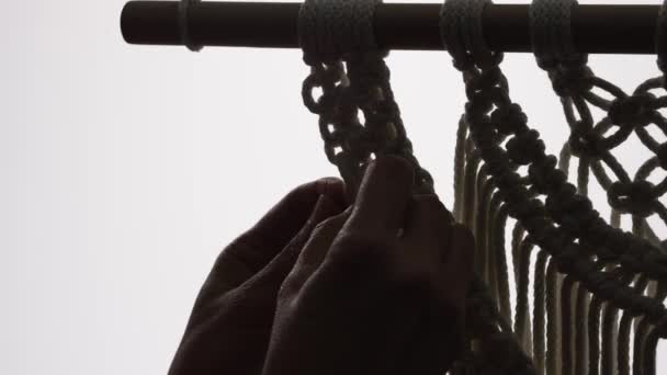 Woman craftsman weaves macrame from light cotton threads. Womens hands knit a beautiful lace ornament from knots on a white background in a darkened home workshop. Close up. Slow motion. — Stock Video