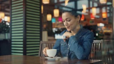 Alışveriş merkezindeki kafede aromatik kahve içen genç bir Afro-Amerikan kadının vitrininden bakın. Bir kadın markalı giyim mağazasında başarılı bir alışveriş yaptıktan sonra dinleniyor. Kapatın. Yavaş çekim.
