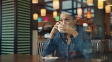Genç Afro-Amerikan kadının telefonla konuşup alışveriş merkezindeki kafede kahvenin tadını çıkardığı cam vitrinlere bakın. Kadın, şirket giyim mağazasında başarılı bir alışveriş yaptıktan sonra dinleniyor. Yaklaştın. Yavaş çekim.