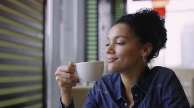 Genç mutlu Afro-Amerikan kadın alışveriş merkezinin kafesindeki masalarda oturmuş aromatik kahvenin tadını çıkarıyor. Moda mağazasından başarılı bir alışveriş yapan bir kadın dinleniyor. Yaklaştın. Yavaş çekim.
