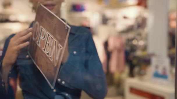 Jonge Afro-Amerikaanse vrouw die een bord van open naar gesloten zet voor de deur van een dameskledingwinkel in een winkelcentrum. De kledingwinkel eindigt zijn werkdag. Sluit maar af. Langzame beweging. — Stockvideo