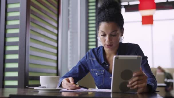 Feminino discutindo projetos e finanças da loja de roupas no café na reunião de vídeo online. Mulher afro-americana usando tablet e gráficos para promover negócios e aumentar as vendas. Fecha. Movimento lento. — Vídeo de Stock