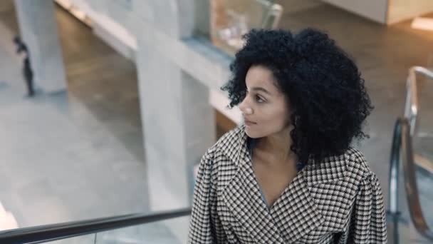 Mujer afroamericana con estilo en un abrigo elegante sube a la escalera mecánica en el centro comercial. Compras, moda y concepto de retail. Gran tienda moderna con ropa y productos de marca. En cámara lenta. De cerca.. — Vídeos de Stock