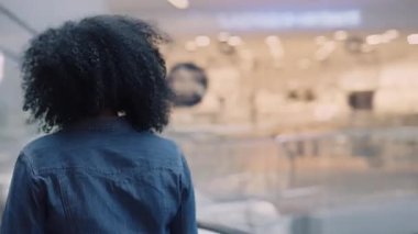 Alışveriş konsepti. Afro-amerikan kadın alışveriş merkezinin arka tarafında yürüyen merdivenden aşağı doğru yürüyen şık bir kadın var. Alışveriş yapmak için bir butikte yürüyen genç bir kadın. Kapat..