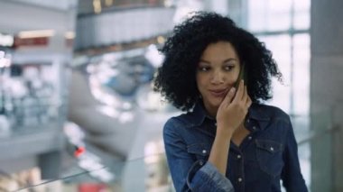 Gülümseyen Afrikalı Amerikalı kadın alışveriş merkezinde telefonla konuşuyor. Marketin önünden şık kıyafetlerle geçen şık bir kadın. Giyim mağazalarından alışveriş yapma kavramı. Kapat..