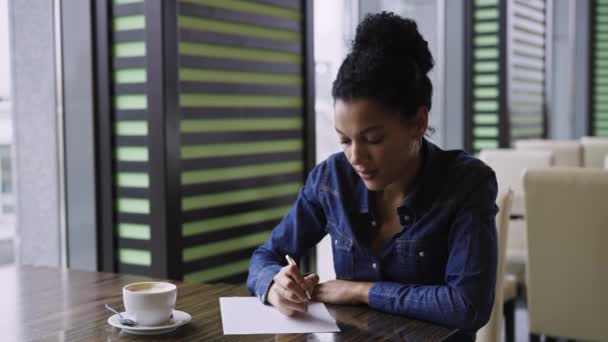 A fiatal afro-amerikai nő álmában gondolkodik valamin, aztán nyikorog egy darab papíron. Egy nő kávézik egy plázában. Vásárlás, tervezés, álmok. Közel volt. Lassú mozgás.. — Stock videók