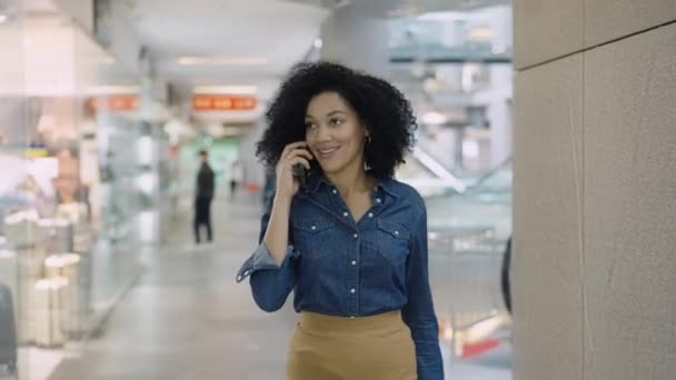 Femme afro-américaine souriante parlant au téléphone dans le centre commercial. Une femme élégante marchant autour du magasin et regardant les vitrines avec des vêtements et des chaussures à la mode. Gros plan. — Video