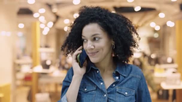 Glimlachende Afro-Amerikaanse vrouw aan de telefoon in het winkelcentrum. Een stijlvolle vrouw loopt rond winkel en kijkt naar de etalages met modieuze kleding en schoenen. Sluiten.. — Stockvideo