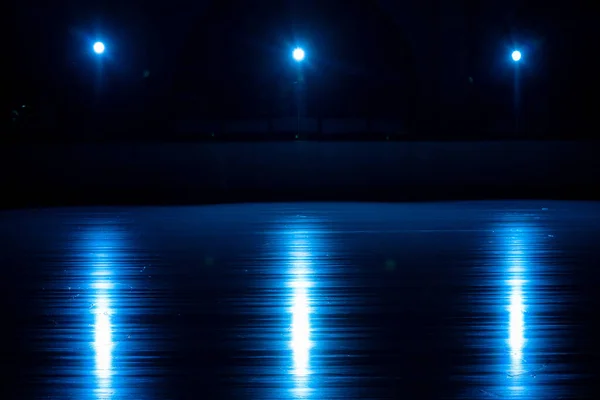 Superficie liscia, lucente di una pista di pattinaggio di ghiaccio con riflesso da riflettori. Palazzina di ghiaccio vuota scura con soffusa luce blu. Concetto di sport invernali giochi, hockey, pattinaggio artistico. Da vicino.. — Foto Stock