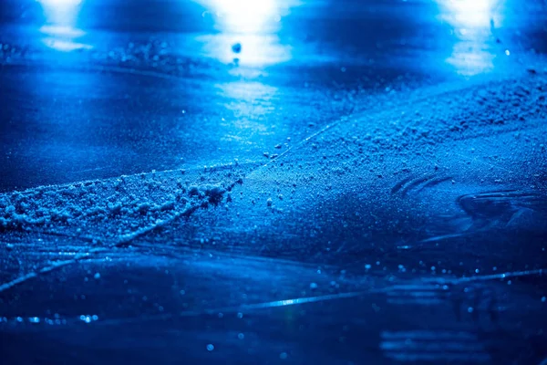 IJsachtergrond en textuur met krassen van schaatsen en hockey. IJsbaan vloer, detail van textuur ijs achtergrond met sneeuw en kristallen in blauw licht. Lege ijsbaan close up. — Stockfoto
