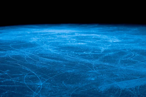Lage hoek op ijsvlak in de arena voor kunstschaatsen of hockey. IJs achtergrond en ijs textuur is gesneden met patroon en krassen van schaatsen. Detail van gestructureerd ijs met sneeuw in blauw licht. Sluiten.. — Stockfoto