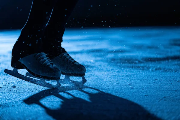 Ben av en idrottare skridskoåkare utför delar av en enda kvinnlig koreografi på isstadion. Ung kvinna genom att öva sina glidande och spinning färdigheter. Konståkning i blått ljus närbild. — Stockfoto