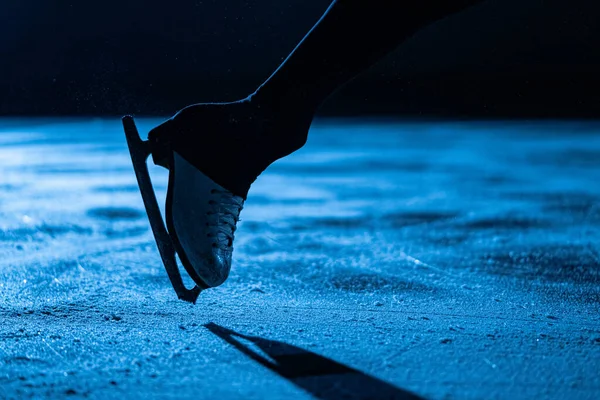 Nogi sportowca łyżwiarza wykonującego elementy choreografii samotnej samicy na stadionie lodowym. Młoda kobieta ćwicząc swoje umiejętności ślizgowe i spinningowe. Jazda figurowa w niebieskim świetle z bliska. — Zdjęcie stockowe