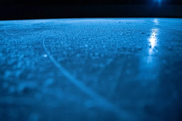 Baixo ângulo na superfície do gelo na arena para patinação artística ou hóquei. Fundo de gelo e textura de gelo é cortado com padrão e arranhões de patins. Detalhe de gelo texturizado com neve em luz azul. Fechar. — Fotografia de Stock