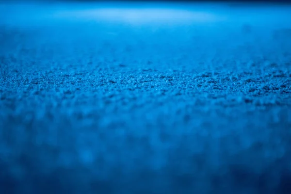 Lav vinkel på isoverflaten i arena for kunstløp eller hockey. Isbakgrunn og isstruktur kuttes med mønster og riper fra skøyter. Detaljer av strukturert is med snø i blått lys. Lukk. – stockfoto