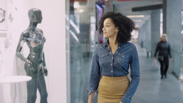 DNYPRO, UKRAINE - DECEMBER 1, 2021: Glad afroamerikansk kvinna går runt köpcentret och tittar på skyltfönstren med märkeskläder. Shopping och mode koncept. Stor modern butik. Närbild. — Stockvideo