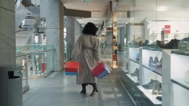 DNYPRO, UKRAINE - DECEMBER 1, 2021: Stylish African American woman is walking through mall with paper shopping bags. Woman rejoices in successful shopping in store with branded clothing. Slow motion. — Stock Video