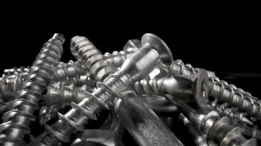 Siyah arka planda dönen çelik krom vidalar yığını. Paslanmaz çelik cıvatalar, masada demir cıvatalar. Metalik sarmal oymacılık. Makro, kapat. Yavaş çekim hazır 59.97fps.
