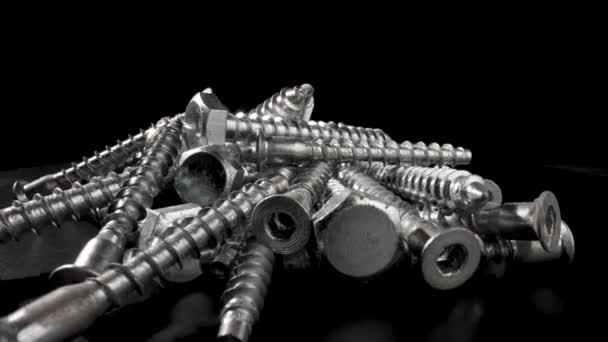 Pile of steel chrome screws rotating on isolated black background. Stainless steel bolts, metal anchor bolts on the table. Metallic helical carving joinery. Macro close up. Slow motion ready 59.97fps. — Stock Video