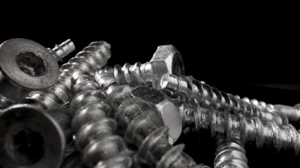 Pile of steel chrome screws rotating on isolated black background. Stainless steel bolts, metal anchor bolts on the table. Metallic helical carving joinery. Macro close up. Slow motion ready 59.97fps. — Stock Video