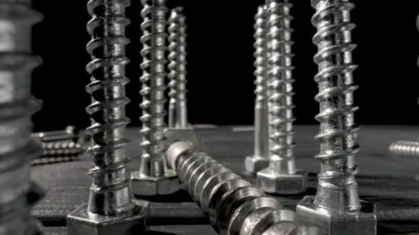 Screws, metal threaded bolts, fasteners on table on isolated black background. Steel chrome anchor screws in workshop or hardware shop. Super macro close up of fixing tools. Slow motion ready 59.97fps — Stock Video