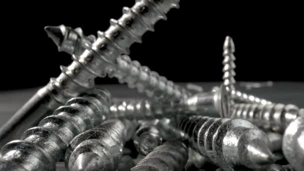 Pile of steel chrome screws rotating on isolated black background. Stainless steel bolts, metal anchor bolts on the table. Metallic helical carving joinery. Macro close up. Slow motion ready 59.97fps. — Stock Video