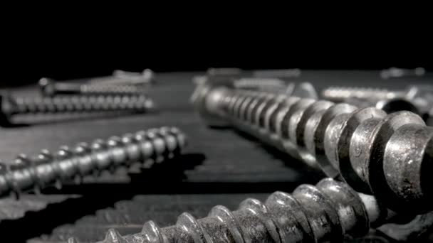 Camera pans over screws, metal threaded bolts, fasteners lying on table on black background. Steel chrome anchor screws in a workshop or hardware shop. Super macro close up. Slow motion ready 59.97fps — Stock Video