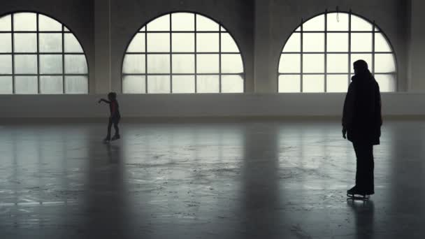 Eiskunstlauftraining. Kleine Eiskunstläuferin übt sich in Spinntechnik auf einem Bein. Trainerin unterrichtet eine Schülerin auf einer dunklen Eisarena mit weichem Licht. Dunkle Silhouetten. Zeitlupe. — Stockvideo