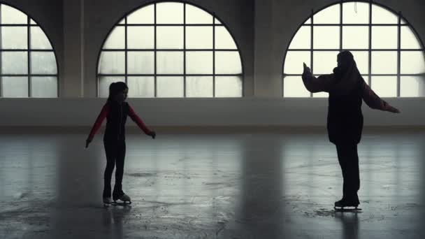 Donna allenatore mostra i suoi elementi studentesca ragazza di pattinaggio artistico coreografia. Ragazza pattinatrice di figura è pattinare e praticare le sue abilità di rotazione di una gamba su arena di ghiaccio scuro. Silhouette. Rallentatore. — Video Stock