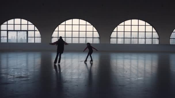 Allenatrice e studentessa che pattinano sull'arena oscura del ghiaccio. Allenatore e giovane pattinatore di figura pratica abilità di spin. Elementi di coreografia di pattinaggio artistico all'arena di pattinaggio. Silhouette. Rallentatore. — Video Stock