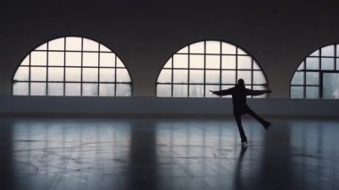 Genç kadın artistik buz pateni koçu koyu buz arenasında paten yapıyor. Dişi artistik patinajcı silueti. Dönme ve kayma becerileri deniyor. Artistik patinaj eğitimi. Yetenek pratiği. Yavaş çekim.