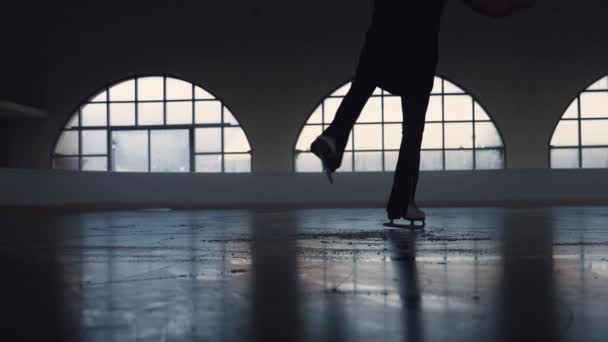 Молодая женщина катается на темной ледяной арене. Закрыть женские ноги на коньках. Фигурист выполняет элементы вращения на льду. Хореография фигурного катания, зимний спорт, тренировки. Медленное движение. — стоковое видео