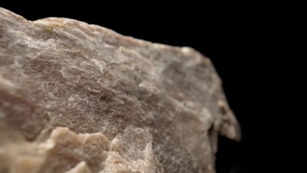 Massief stuk graniet of kwartssteen tegen een zwarte achtergrond. Natuurlijk ruw mineraal. Achtergrond van de natuurlijke structuur van steen. Begrip geologie, ertswinning, bouwmateriaal. Macro close-up. — Stockvideo