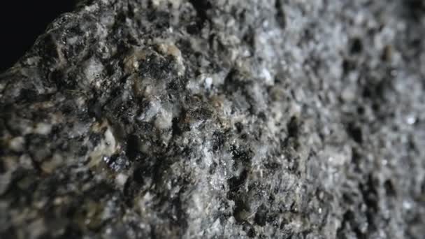 Ιστορικό φυσικής πέτρινης υφής γκρίζου ακατέργαστου γρανίτη. Ένα κομμάτι πέτρας με ανάγλυφο μοτίβο σε μαύρο φόντο στούντιο. Μεταλλική πέτρα για κατασκευές. Γεωλογία, μετάλλευμα, πόροι. Μακρό κλείσιμο. — Αρχείο Βίντεο