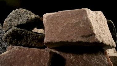 Katı, sert granit taş parçaları siyah bir stüdyonun arka planında dönüyor. Kahverengi ve gri granit veya kuvars mineralleri. İnşaat için taşlar. Jeoloji, cevher, kaynaklar. Doğal taşlar kapanır..