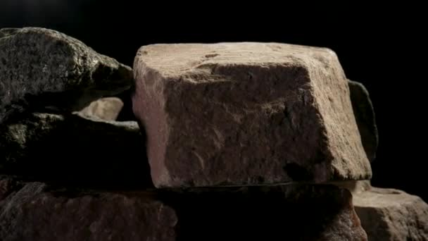 黒いスタジオの背景に回転する固い花崗岩の石の破片。褐色や灰色の花崗岩や石英鉱物。建設のための石。地質学、鉱石、資源。天然石が近くに. — ストック動画