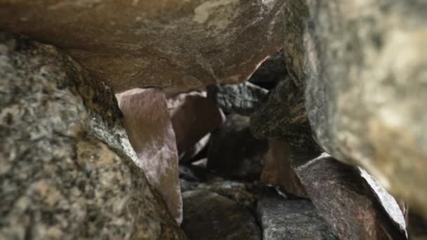 Kamera, gri ve kahverengi granit taşlardan oluşan bir yığının içinde siyah bir arkaplana doğru hareket ediyor. Sert granit çakıl taşları, doğal dokusu ve kırık şekilleri var. Jeoloji. Taş geçidi. Yaklaş.. — Stok video