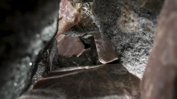 Camera pans inside a pile of gray and brown granite stones against a black background. Rough granite gravel cobblestones with natural texture and fracture patterns. Geology. Stone gorge close up. — стоковое видео