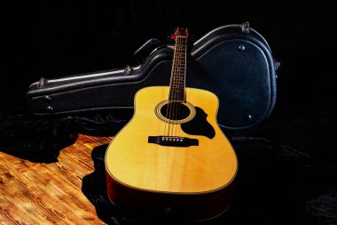 Tahta sarısı akustik gitar ahşap zeminde, sert bir çantanın yanında duruyordu. Siyah açık gardırop bagajının yanında telli müzik aleti. Telli müzik aleti. Kapat..