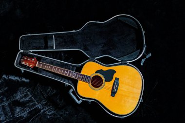 Tahta sarısı akustik gitar sert bir çantada duruyor. Siyah bir gardırop bagajında telli müzik aleti. Rock, country, folklor icra eden telli bir müzik aleti. Kapat..
