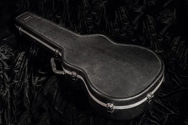Fekete keménytok a fekete velúr szöveten fekvő gitárhoz. Zárt burkolat egy húros hangszerhez közelről. Fekete szekrény láda akusztikus gitárhoz. — Stock Fotó