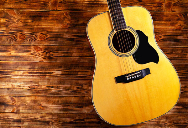 Classical acoustic guitar on a wooden background. Yellow stringed musical instrument for playing chords and melodies on the strings. Background for music school, learning to play the guitar. Close up.