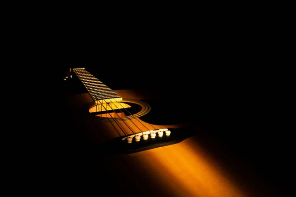 A fénysugár megvilágítja a sárga fa akusztikus gitárt. Vonós hangszer fekete háttérrel a sötétben. Hangszer akkordok és dallamokat játszani a húrokon. Gitár közelről — Stock Fotó