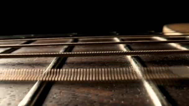 Slider macro shot από ακουστικό λαιμό κιθάρας με μεταλλικά έγχορδα και χαλινάρια σε μαύρο φόντο. Κλασσικές χορδές κιθάρας δονούνται όταν παίζετε τραγούδι. Καφέ ξύλινη σανίδα μιας κιθάρας ακραία από κοντά. — Αρχείο Βίντεο